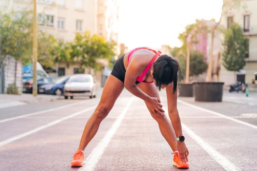 unrecognizable sportswoman stretching legs on the athletics track of the city during her training, concept of urban sport and healthy lifestyle, copy space for text
