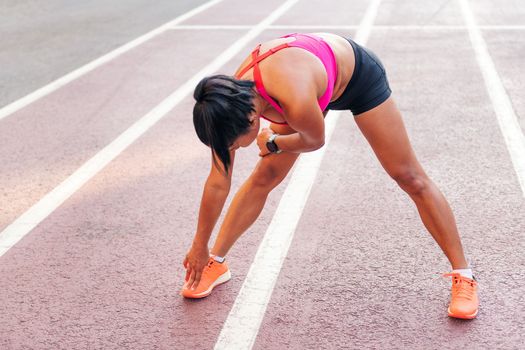 unrecognizable sportswoman stretching legs on the athletics track during her training, concept of urban sport and healthy lifestyle, copy space for text