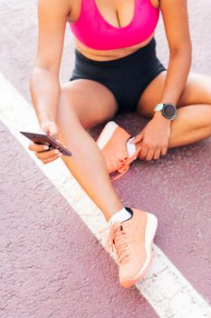 unrecognizable female athlete using her mobile phone sitting on the athletics track after her workout, concept of sport and healthy life style, copy space for text