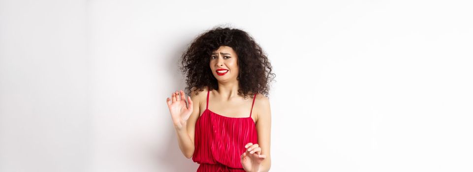 Young woman cringe of something creepy, grimacing and recoil from disgusting awful thing, standing in red dress on white background.