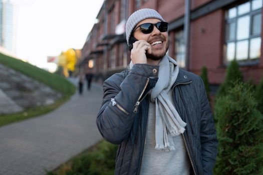 stylish fashionably dressed man talking on the phone outside wearing sunglasses.