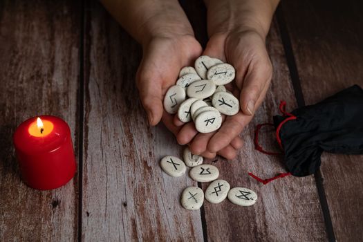 woman's hands teaching rune stones with black symbols for fortune telling on a wooden table