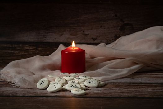 rune stones with black symbols for fortune telling with candles on a wooden table