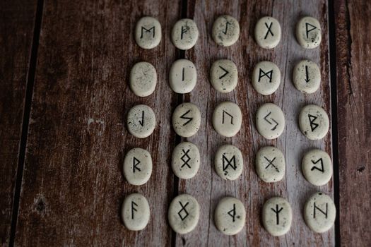 rune stones with black symbols for fortune telling with candles on a wooden table