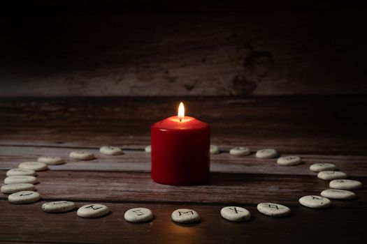 rune stones with black symbols for fortune telling with candles on a wooden table