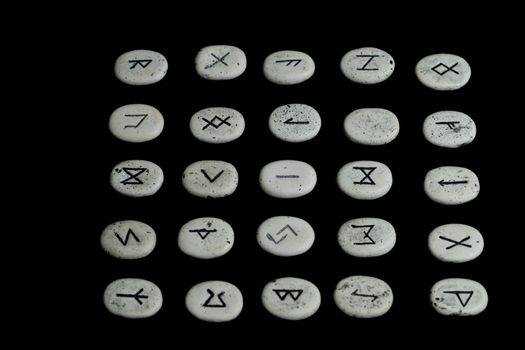 rune stones with black symbols for fortune telling with candles on a wooden table