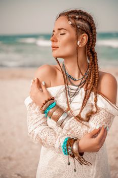 Model in boho style in a white long dress and silver jewelry on the beach. Her hair is braided, and there are many bracelets on her arms