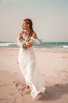 Model in boho style in a white long dress and silver jewelry on the beach. Her hair is braided, and there are many bracelets on her arms