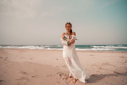 Model in boho style in a white long dress and silver jewelry on the beach. Her hair is braided, and there are many bracelets on her arms