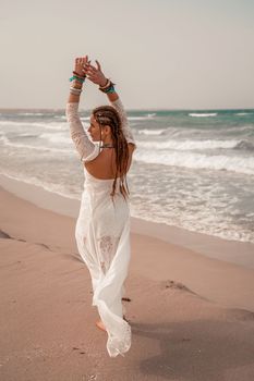 Model in boho style in a white long dress and silver jewelry on the beach. Her hair is braided, and there are many bracelets on her arms