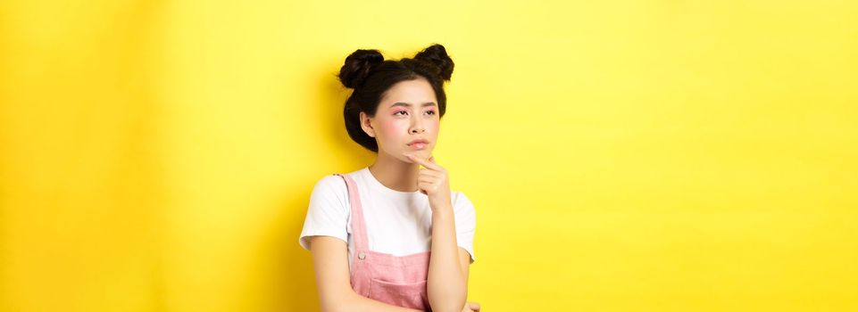 Thoughtful serious girl with beauty makeup, looking left and thinking with suspicious face, have doubts, standing on yellow background.