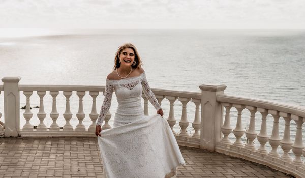 Romantic beautiful bride in white dress posing with sea and mountains in background. Stylish bride standing back on beautiful landscape of sea and mountains on sunset