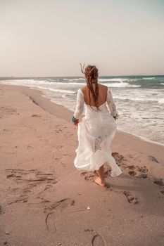 Model in boho style in a white long dress and silver jewelry on the beach. Her hair is braided, and there are many bracelets on her arms