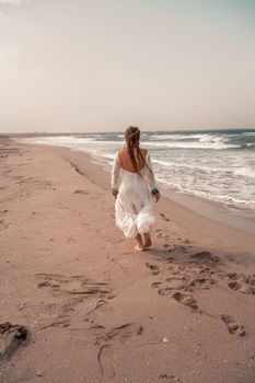 Model in boho style in a white long dress and silver jewelry on the beach. Her hair is braided, and there are many bracelets on her arms