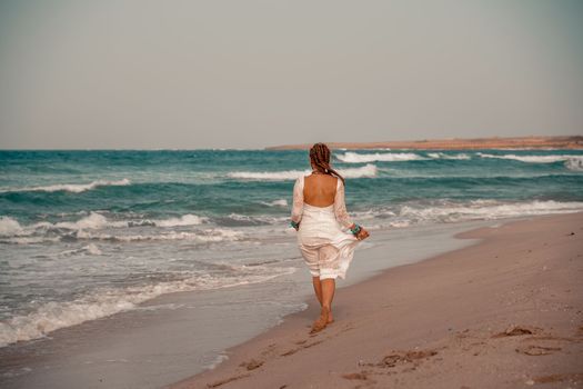 Model in boho style in a white long dress and silver jewelry on the beach. Her hair is braided, and there are many bracelets on her arms