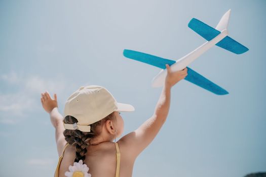 Kid playing with toy airplane. Children dream of travel by plane. Happy child girl has fun in summer vacation by sea and mountains. Outdoors activities at background of blue sky. Lifestyle moment