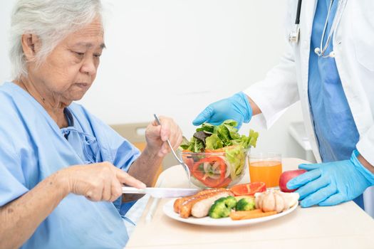 Asian senior or elderly old lady woman patient eating breakfast and vegetable healthy food with hope and happy while sitting and hungry on bed in hospital.