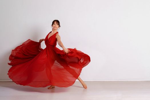 Dancer in a red flying dress. Woman ballerina dancing on a white studio background.