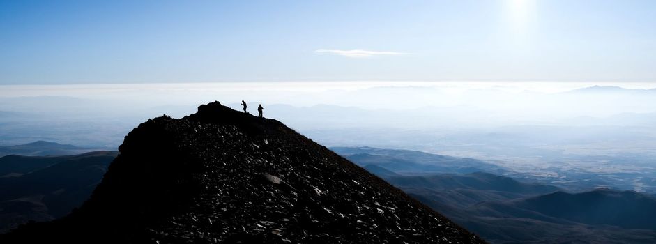 Silhouette of hikers on mountain top on clear sky background, panoramic view