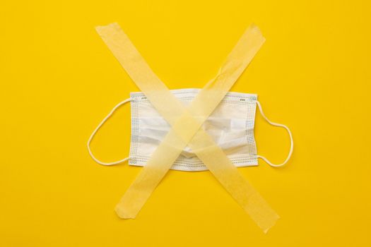 Medicine mask sticked up with masking tape isolated on yellow background with copy space. Concept of pandemic restrictions during covid coronavirus time. Stay safe and care about people health