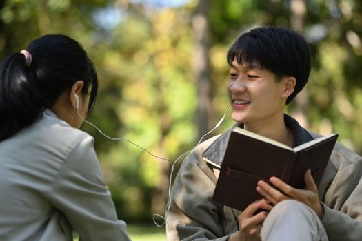 Romantic young couple listening to music with earphones while relaxing in nature park on beautiful day.