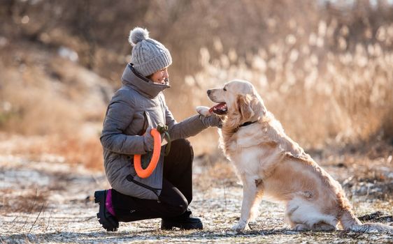 Woman owner holding paw of golden retriever dog during early spring walk outdoors and smiling looking at him. Girl with doggy pet labrador together at the nature