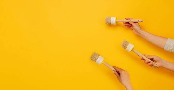 Three hands holding paint brushes on yellow background with copy space. Concept of creativity, improvement and renovation. Working tool