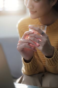 Beautiful business woman working with a laptop while drinking glass of water at home.