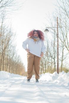 Smiling plump redhead woman jumping in park in winter