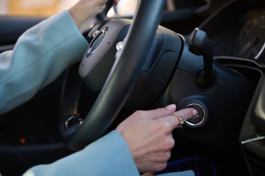 Close-up woman finger pressing the start stop engine button on modern car. Woman driver pushing a start ignition button switch in the automobile. Driving car. Concept of transportation and technology