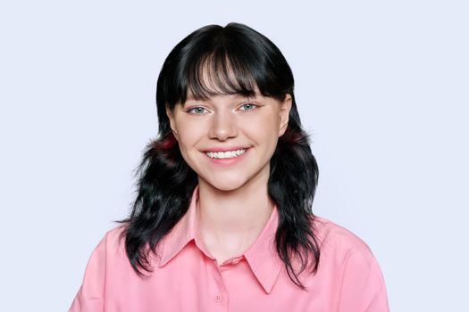 Portrait of happy smiling young female looking at camera on light studio background. Attractive girl posing, in pink shirt with toothy smile. Beauty, health, facial skin care teeth