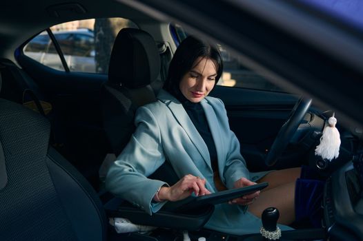 Confident Caucasian businesswoman sitting on driver's seat, using digital tablet, working on new project, telecommuting, planning meeting with colleagues. Lifestyle People Remote work business concept