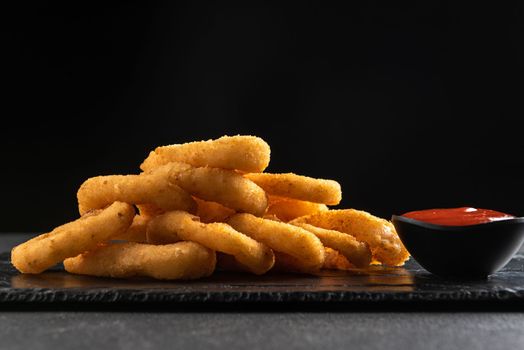 Calamari rings deep-fried in breading. Crispy squid rings on a dark background with sauce