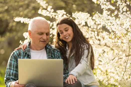 grandfather and granddaughter with laptop in the garden.