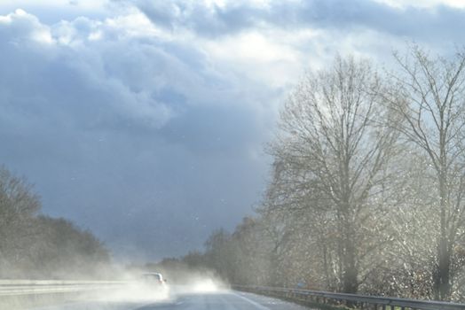 Wet highway with trees at the side against a dramatic sky