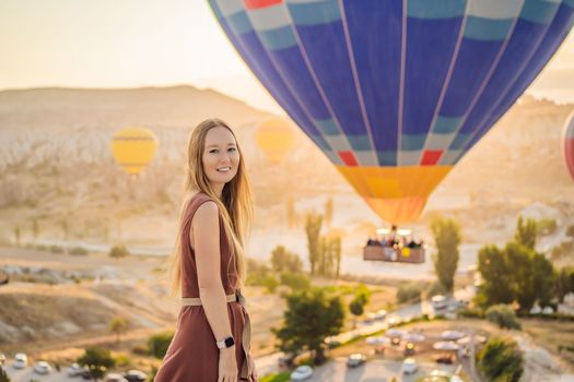 Tourist woman looking at hot air balloons in Cappadocia, Turkey. Happy Travel in Turkey concept. Woman on a mountain top enjoying wonderful view.