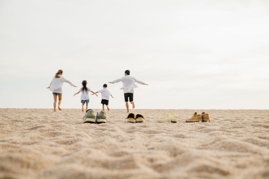 Happy family day. lifestyle father, mother and kids take off shoes running on sand, Back view Asian having family parents with child fun holding hands together run to beach, tropical summer vacations