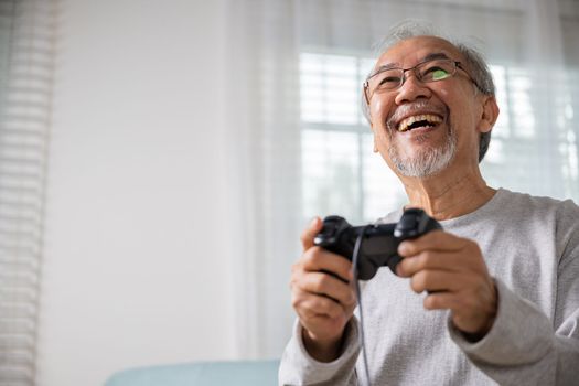 Funny retirement elderly smile sitting on sofa life gaming, lifestyle senior old man enjoying holding joystick playing video game at home, gamer mature man hands using game controller play videogame