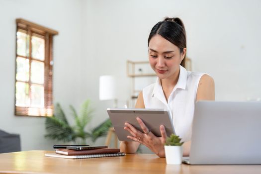 Portrait of young asian woman holding stylus pen while working on tablet computer at home.