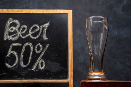 an empty beer glass on a wooden table on a dark background. A glass for craft beer. blackboard with price list. High quality photo