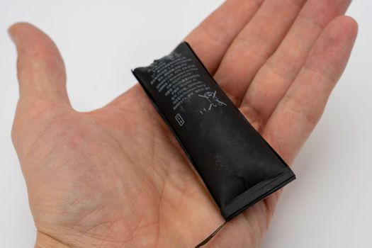 A swollen faulty smartphone battery in the hand of a smartphone repairman. Damages and malfunctions of mobile phones. Smartphone repair. Replacing the battery in a mobile phone