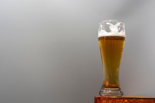 A glass of fresh and cold beer on a wooden table on a grey background. A glass of light craft beer.