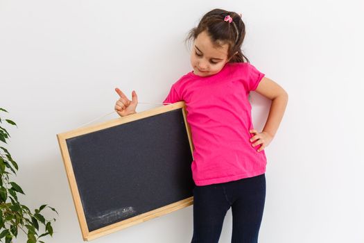 Smiling Little School Girl Holding Blank Chalk Board with Copy Space.