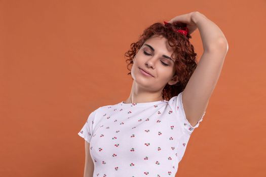 Curly chestnut-colored hair. A woman corrects her hair gently with her hand. White blouse with a cherry pattern. Isolated from the uniform background.