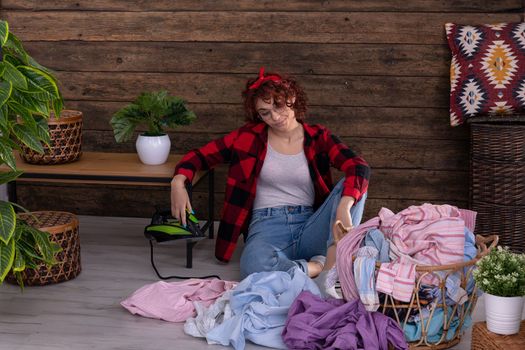 A girl with curly hair, tired of endless housework like laundry and ironing. A wall of brown boards in the house.