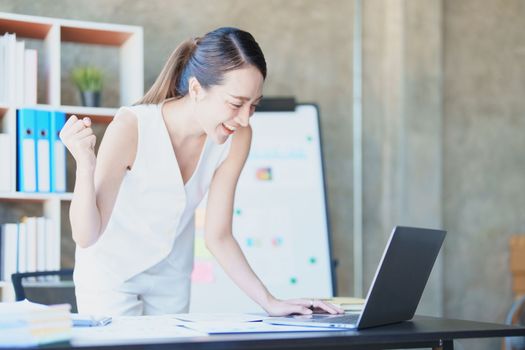 Portrait of a woman business owner showing a happy smiling face as he has successfully invested her business using computers and financial budget documents at work.