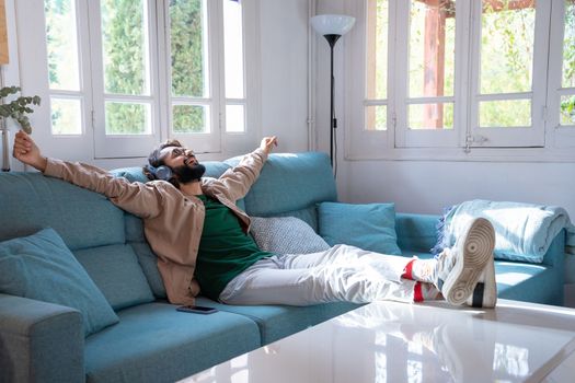 young relaxed man listening to music or podcast with headphones lying on the sofa at home. High quality photo