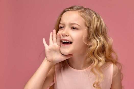 Nice little girl with a blond curly hair, in a pink dress is screaming, on a pink background