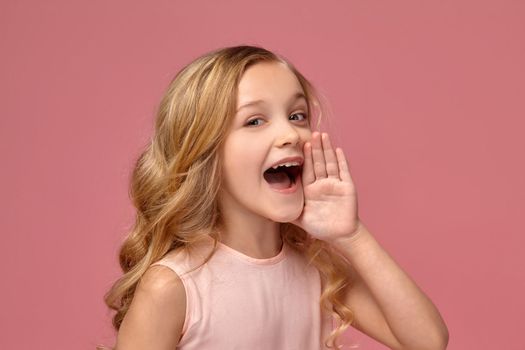 Charming little girl with a blond curly hair, in a pink dress is screaming, on a pink background