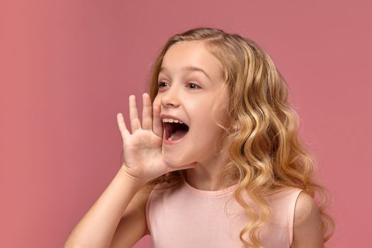 Wonderful little girl with a blond curly hair, in a pink dress is screaming, on a pink background